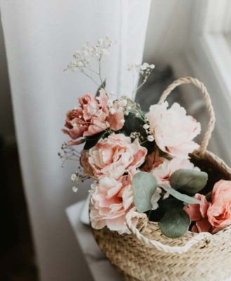 enviar cesta de flores para regalar cesta de mimbre con peonia rosada, paniculata y hojas verdes sobre mesa blanca vista cenital